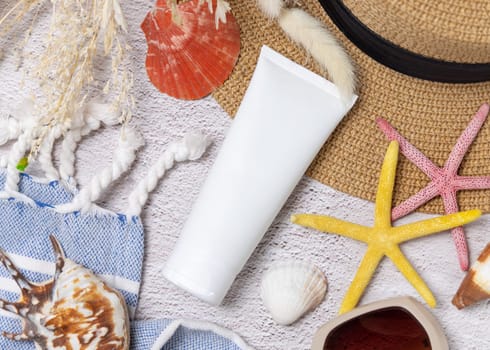White blank cream squeeze tube on hat bag near towel, seashells and starfishes top view. Sunscreen cosmetics mockup. Summer vacation with spf uv-protected sunbathing