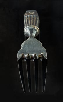 Perspective surface view of Ancient vintage fork isolated on black background. Close-up of Black worn metal vintage fork in dark tone, Highlighting its texture and design, use it as your Space for text, Design, Wallpaper and Poster, Selective focus.
