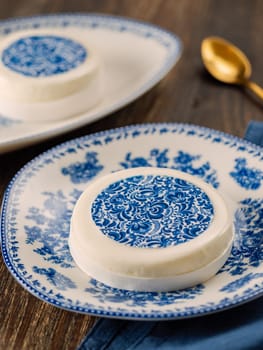 Pastry dessert in Gzhel rustic style. Sweet pastry decorated blue flowers photo printing on sugar paper. Mini cake Gzhel on plate over wooden tabletop background. Closeup. Vertical