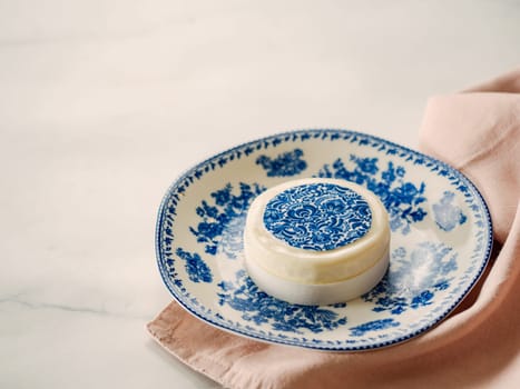 Pastry dessert in Gzhel rustic style. Sweet pastry decorated blue flowers photo printing on sugar paper. Mini cake Gzhel on plate over white marble tabletop background. Copy space.