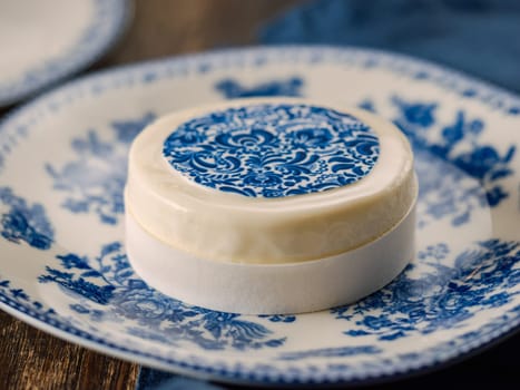 Pastry dessert in Gzhel rustic style. Sweet pastry decorated blue flowers photo printing on sugar paper. Mini cake Gzhel on plate over wooden tabletop background. Closeup