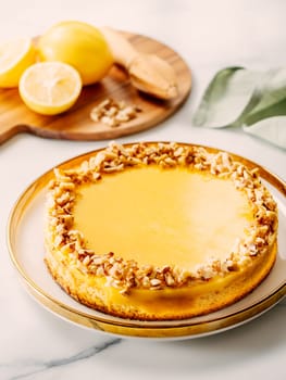 Perfect lemon tart or cake, modernly decorated chopped walnuts. Delicious whole lemon pie on plate on white marble table background. Aesthetic of traditional classic french lemon tart, recipe idea
