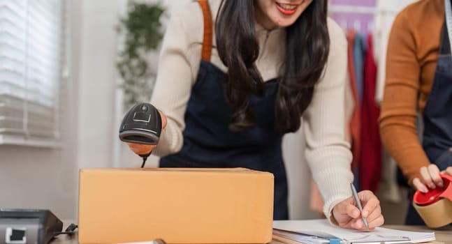 An e-commerce employee scanning a package for inventory management while taking notes in a retail store setting.