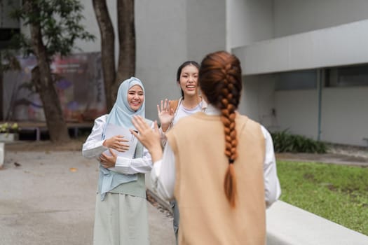 A group of diverse university students happily greeting a friend with smiles and waves while enjoying their time on campus.