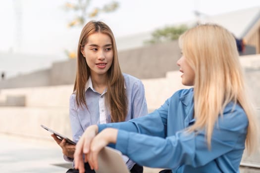 Two diverse women engaged in a friendly conversation while one holds a tablet, fostering collaboration in an outdoor environment.