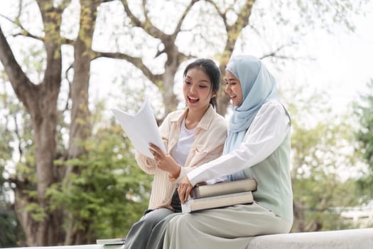 Diverse female students excitedly discussing their study materials, holding notes and books while seated together in a peaceful university park environment.