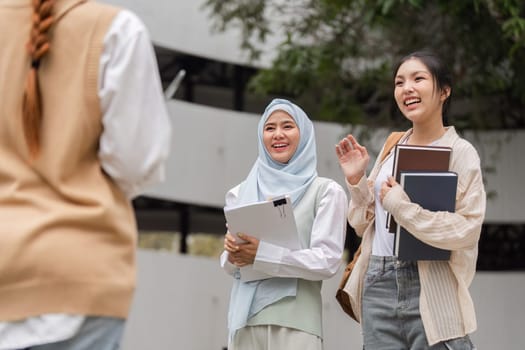 Two diverse female students greeting a third friend with smiles, sharing joy and holding their study materials in an outdoor campus setting.