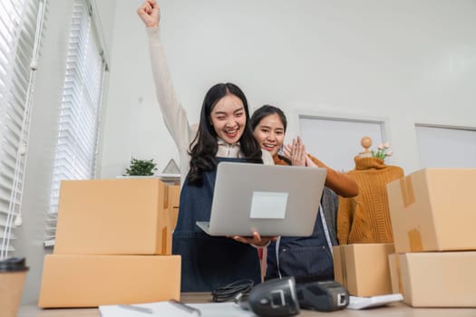 Two diverse retail workers joyfully celebrating an achievement with one raising their fist in excitement while using a laptop in a retail environment.