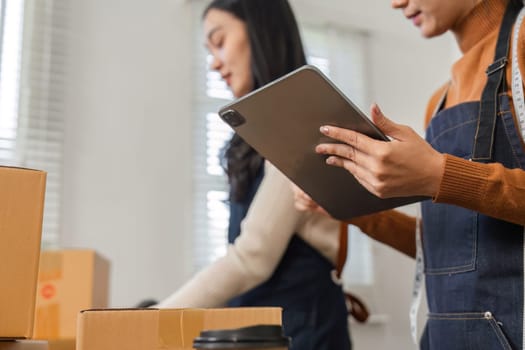 Two diverse warehouse workers collaborating to organize packages and manage inventory using a tablet in a logistics environment.