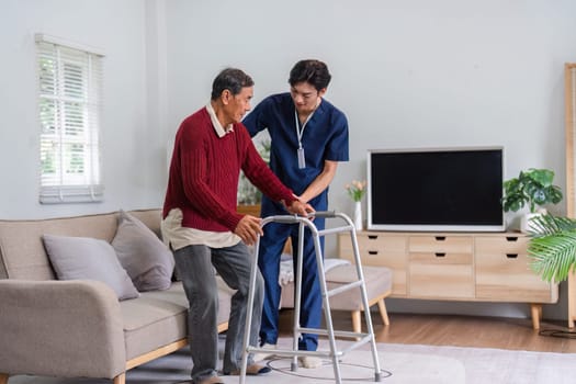 A caring nurse smiles as he supports an elderly man with a walker in a bright living room, fostering a positive atmosphere for rehabilitation.
