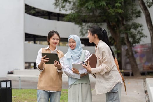 A group of diverse university students gathered outdoors, collaborating and discussing academic projects while using a tablet.