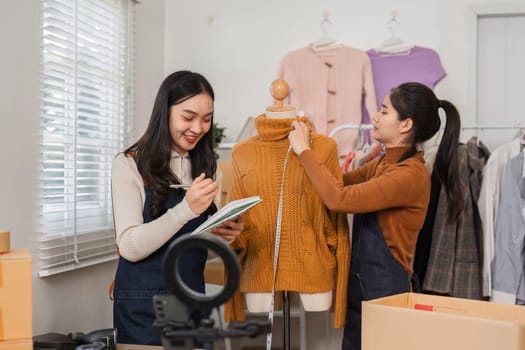 Two diverse retail workers collaborating to take notes and adjust a sweater on a mannequin while organizing inventory in a fashionable retail setting.