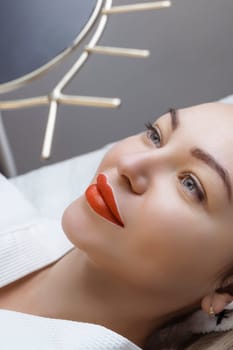 Permanent lip tattooing. A sexy girl with beautiful lips looks into the mirrors lying on the couch at the cosmetologist.