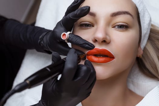 Cosmetologist makes permanent makeup on a woman's face. Specialist applies a tattoo on the patient's lips close-up.