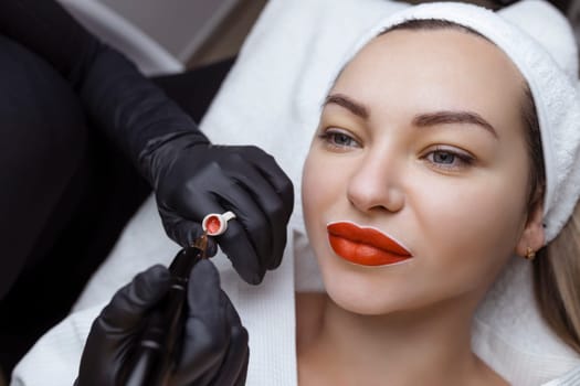 Cosmetologist makes permanent makeup on a woman's face. Specialist applies a tattoo on the patient's lips close-up.