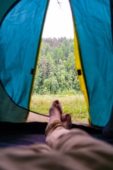 Pov shot capturing a camper relaxing inside a tent, soaking in the stunning view of a lush green forest and serene surroundings