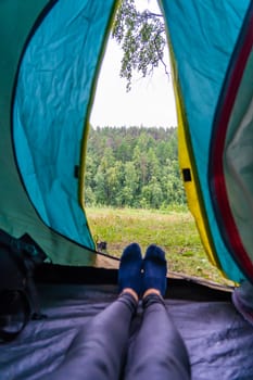 Woman relaxing inside a tent with feet up, soaking in the breathtaking view of a lush green forest and enjoying the tranquility of nature