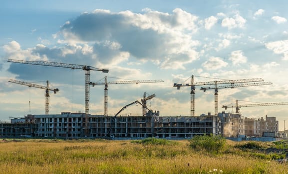 Construction cranes rising against sunset sky, developing multi story residential complex with urban architectural progress