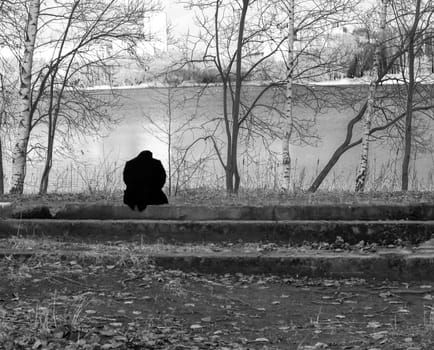 Conceptual, black and white shot of the person sitting by the bank of the river