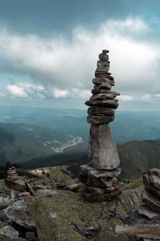 A carefully balanced stone cairn stands tall on a rocky outcrop, with expansive mountain ranges in the background. The clear sky enhances the sense of openness and freedom.