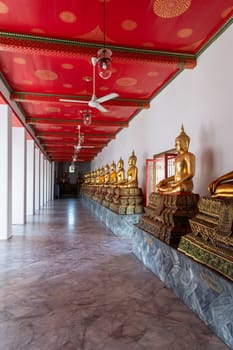 A tranquil corridor in a Buddhist temple, featuring golden statues and a vividly colored red ceiling