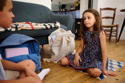 Two children with their school backpacks at home share a moment, emphasizing learning and a cozy environment.