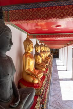 A tranquil corridor in a Buddhist temple, featuring golden statues and a vividly colored red ceiling