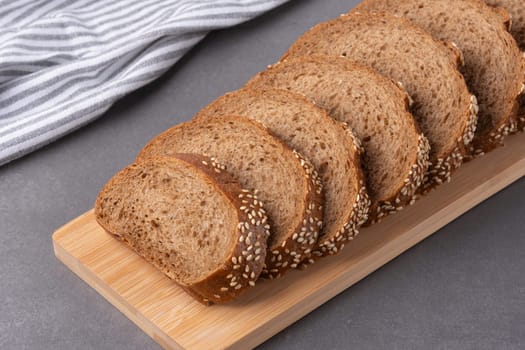Freshly sliced sesame seed bread on a wooden cutting board with a striped kitchen towel in the background in a modern kitchen.