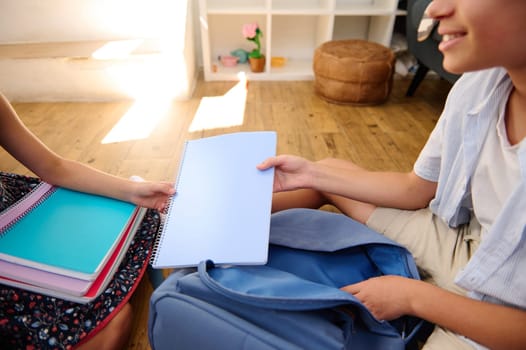 Two people sitting on a wooden floor sharing notebooks, depicting teamwork and study environment.