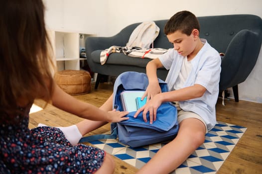 Two children organize school supplies with focus and teamwork, sitting on a mat in a cozy room.