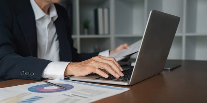 An elderly businessman reviews important reports on his laptop emphasizing the significance of diligence in a professional setting.
