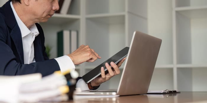 An elderly businessman reviews data on a tablet in a sleek office reflecting on strategic decisions in a digital age.