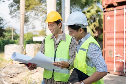 Two logistics engineers discuss project plans at a construction site emphasizing teamwork and project management in action.