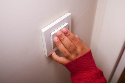 A child in a red sweater is about to switch on the light in a room.