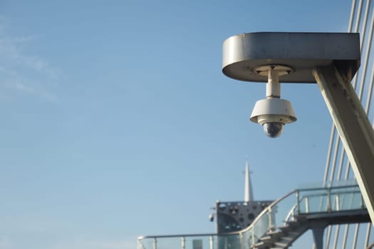 A security camera is installed on a bridge with a blue sky above.