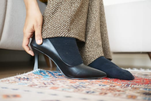 A person carefully puts on elegant black high heels while seated.
