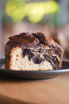 A slice of marbled cake sits on a black plate in a warm cafe setting.