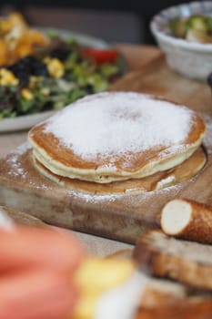 Fluffy pancakes dusted with sugar sit next to a colorful salad.
