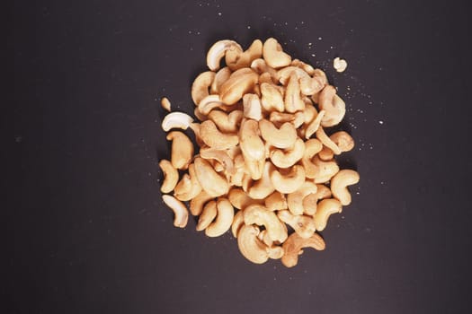 A pile of cashew nuts is displayed on a dark surface, highlighting their shape.