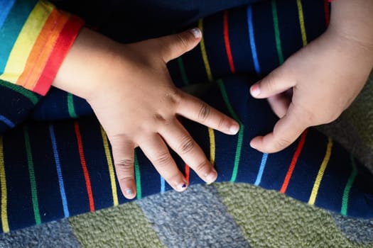 Small hands rest on vibrant striped socks while seated on a textured carpet.