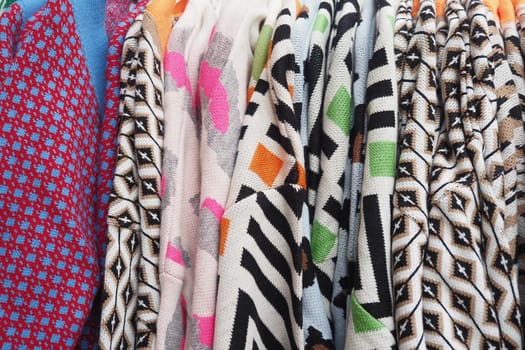 Knitted sweaters in various colors hang bright at an outdoor market stall.