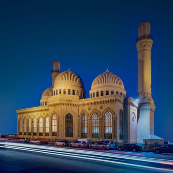Nighttime view of Bibi-Heybat Mosque in Baku, Azerbaijan, showcasing its illuminated domes and intricate design. The surrounding cars add to the lively atmosphere