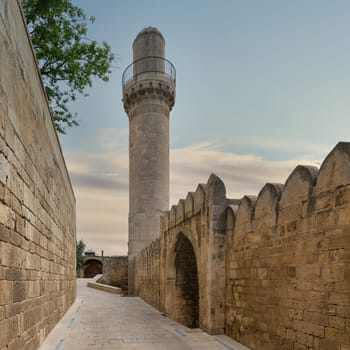The minaret of the Shah Mosque rises above the surrounding buildings in Baku, Azerbaijan before sunset. The mosque is connected to the Palace of the Shirvanshahs and is a notable landmark in the city