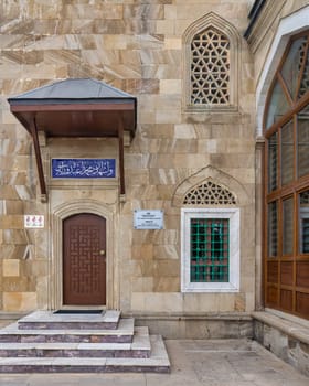 Side entrance of Sehitler Mosque in Baku, Azerbaijan, featuring a stone facade adorned with intricate Islamic architectural details. The entrance boasts an ornate doorway and windows