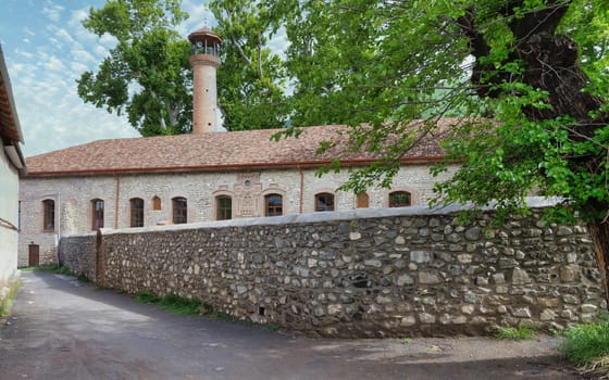 Exterior view of Shaki Khan's Mosque Complex, a historic structure located in Shaki, Azerbaijan, characterized by its minaret, arched windows, stone walls, and traditional architectural elements