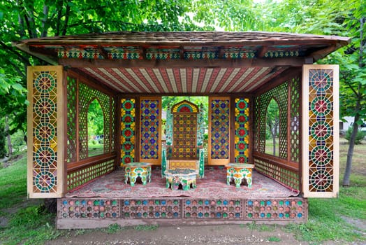 A vibrant and intricately designed pavilion features ornate decor and colorful patterns, nestled in a garden area near Shaki Khan Palace in Azerbaijan