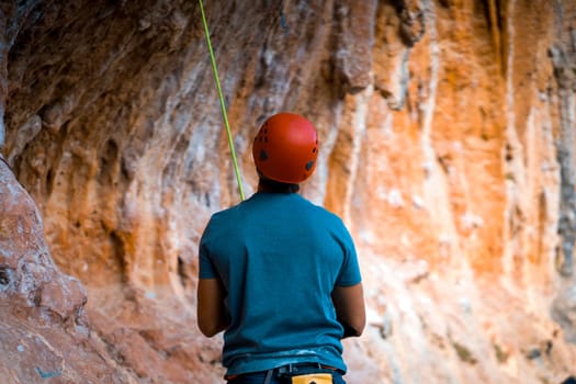 The silhouette of a rock climber in a red helmet, a man stands against the background of a rock and prepares to start, to train in the mountains on a sunny day.