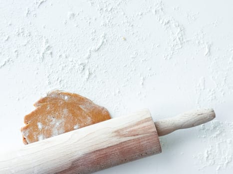 Rustic wooden rolling pin with cookie dough on floured surface.