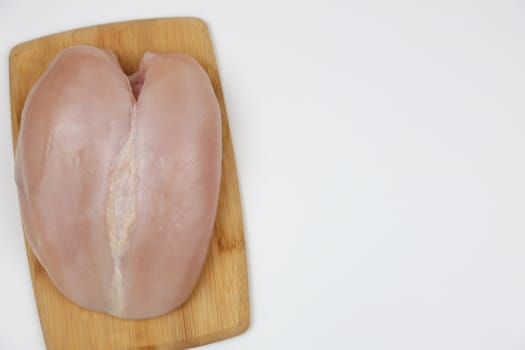 Close-up view of chicken fillet from above lying on a wooden cutting board on a white background with space for text. The concept of cooking, dietary menu, healthy and natural products. High quality photo