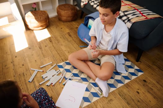 Child sitting on the floor, surrounded by markers, enjoying artistic activities in a cozy, sunlit living room setting.